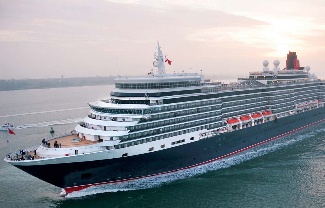 The queen Elizabeth cruise ship sailing by a misty coast as the sun sets