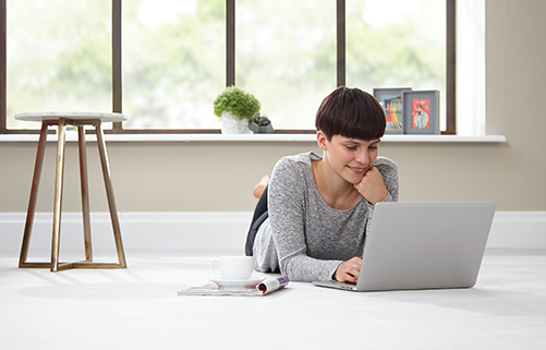 A woman lying on a floor fitted with an airborne sound reducing underlay on her laptop