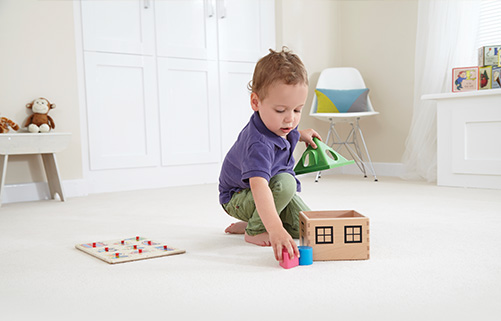 A toddler playing with his toy house on a floor fitted with an extra comfortable underlay