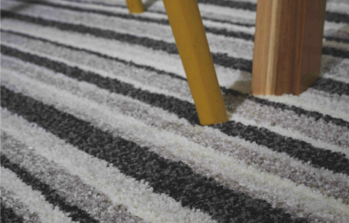 a light brown wooden chair leg on a striped black and white carpet with a good underlay